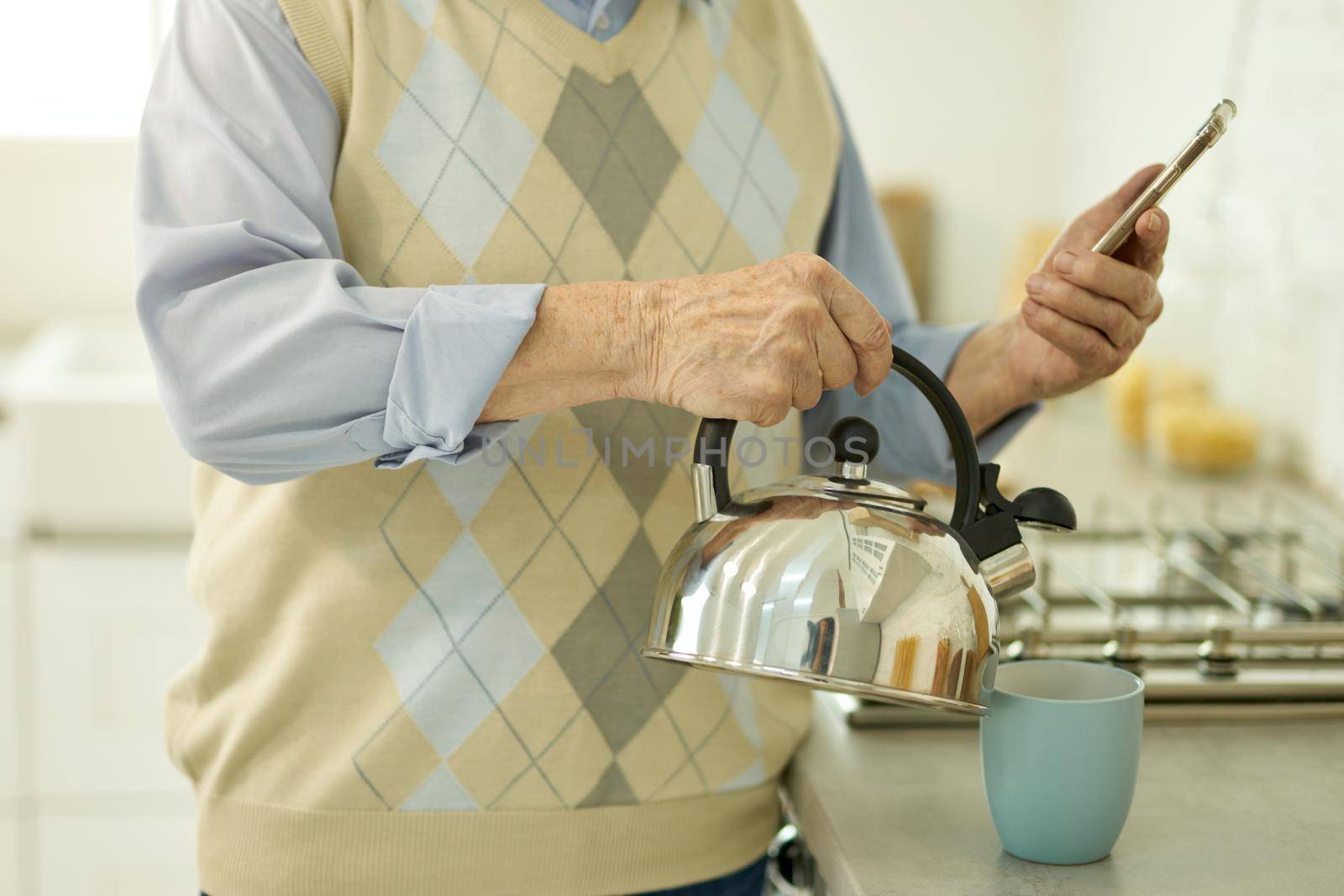 Aged man looking and smartphone and pouring water from kettle by friendsstock
