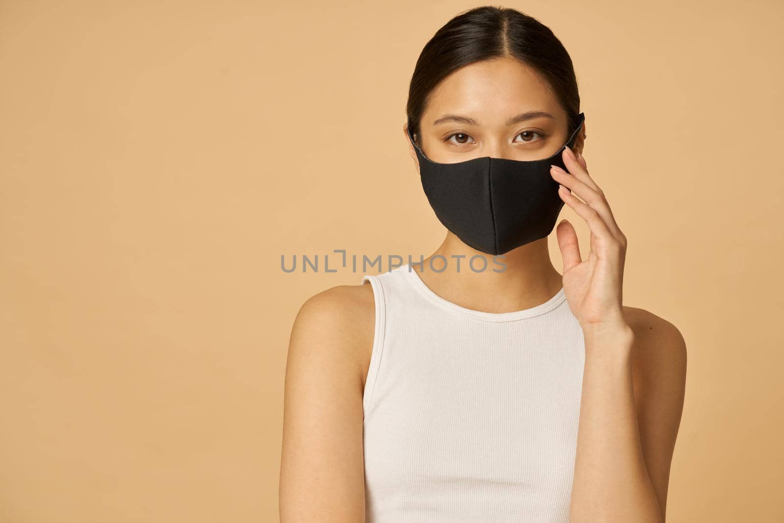 Charming young woman wearing black facial mask looking at camera, posing isolated over beige background. Safety, pandemic concept