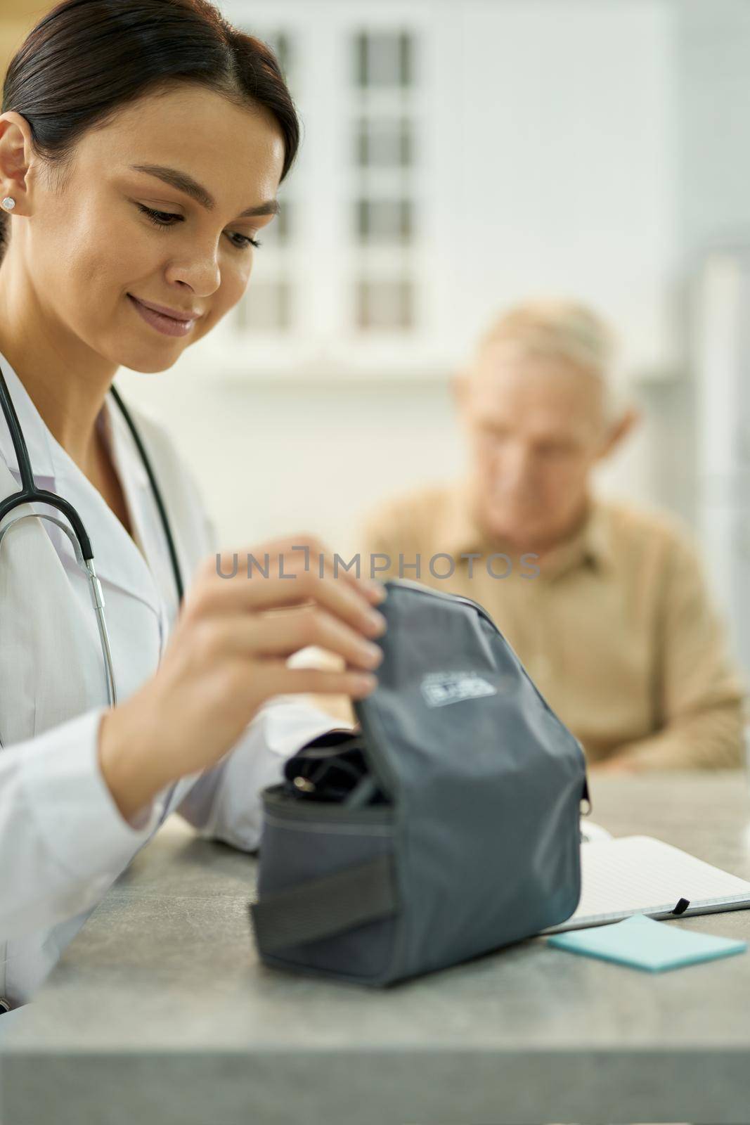 Friendly medical worker smiling while opening a dark bag with medical equipment