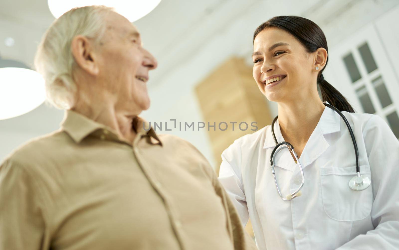 Friendly lady in white lab coat smiling at a senior citizen in her medical care