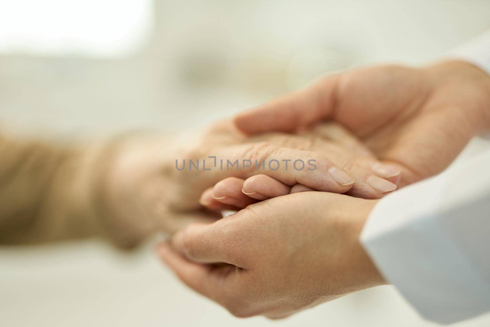 Caring doctor holding and examining hand of a senior patient by friendsstock