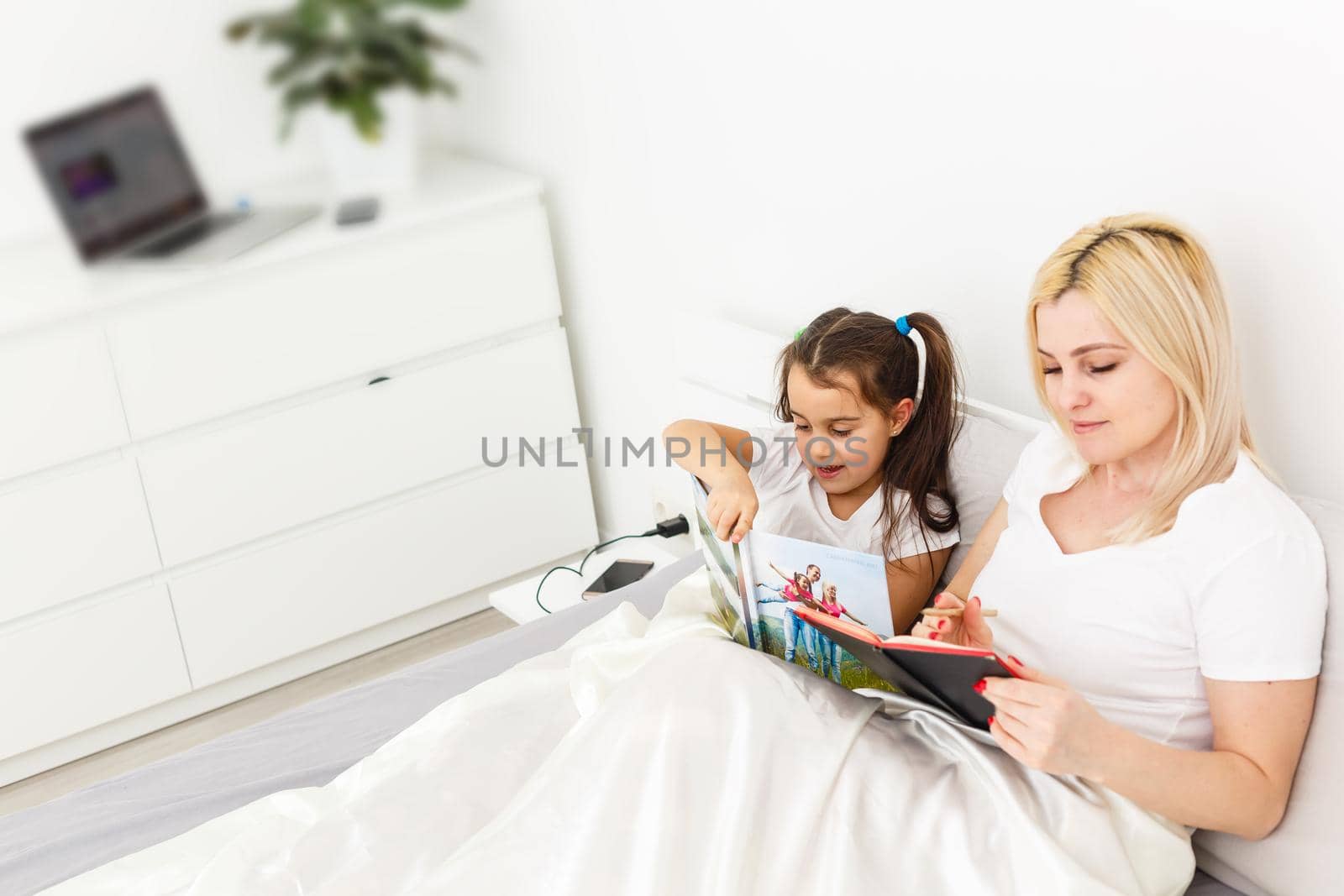 Cute little girl and her mother lying on a bed.