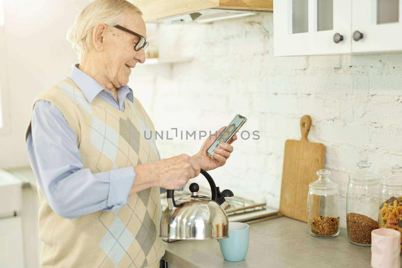 Smiley elderly gentleman making tea and consulting his doctor online by friendsstock