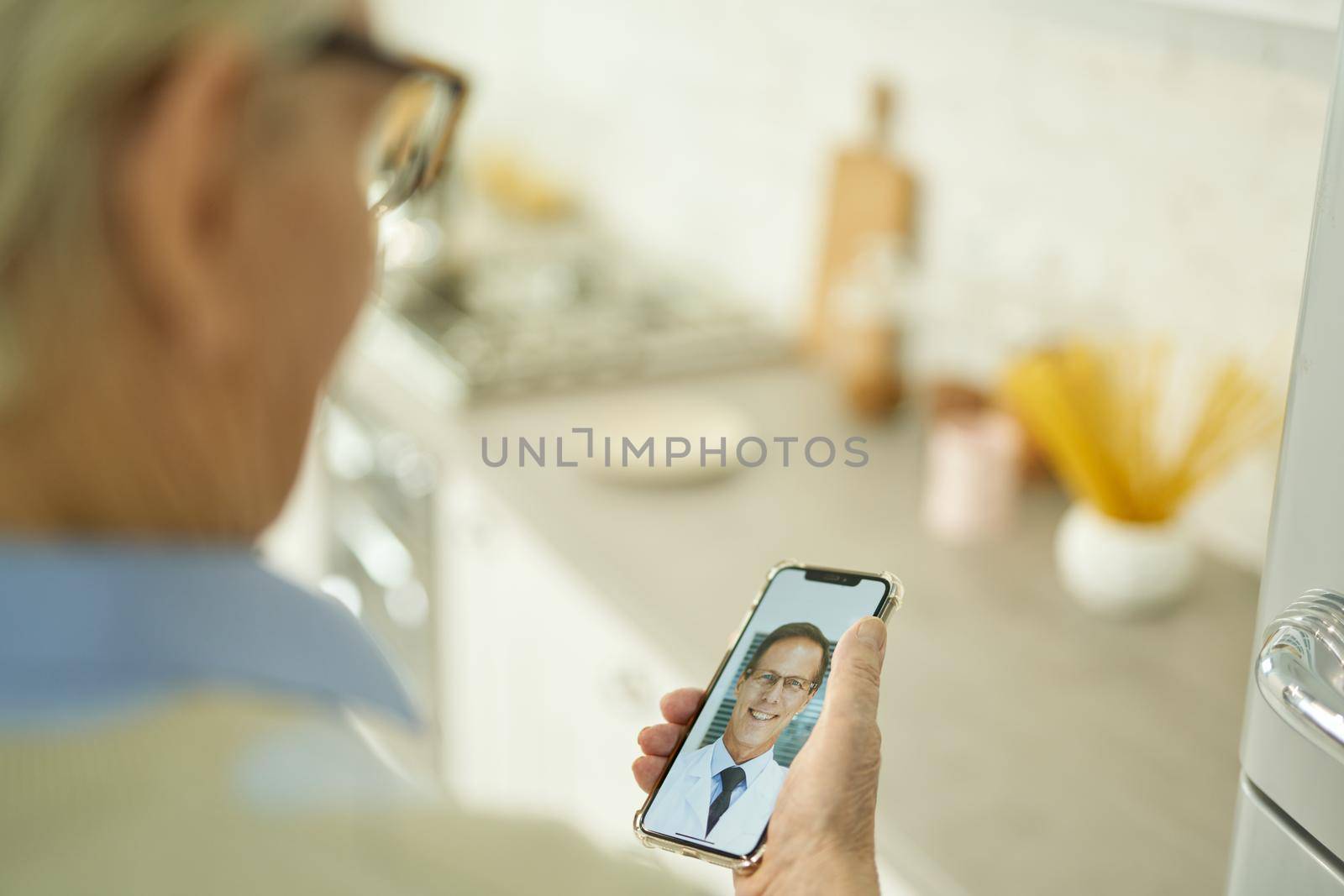 Cropped photo of grey-haired man in glasses holding a smartphone and video-calling his medical doctor