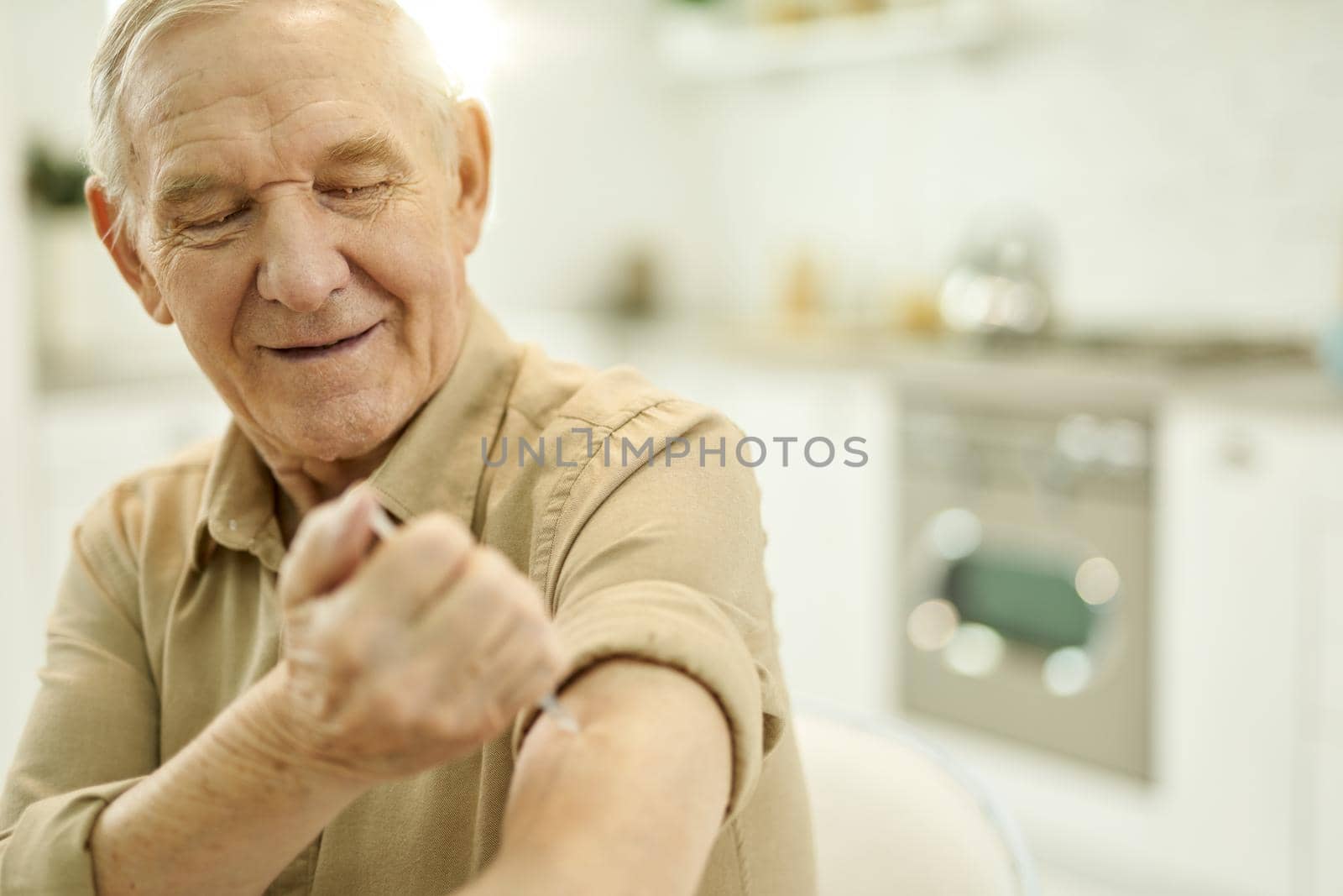 Independent senior man giving himself an arm injection by friendsstock