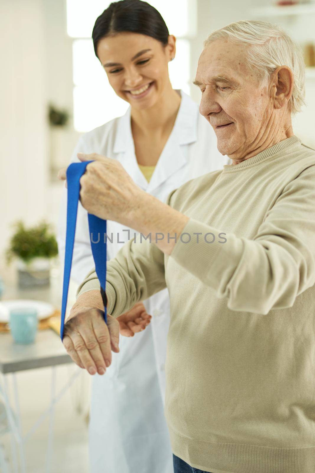 Smiling elderly man and young nurse looking at fitness rubber by friendsstock