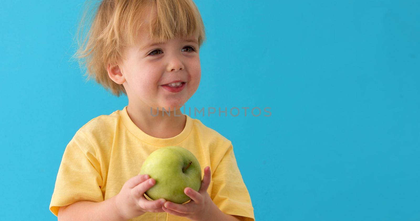 small boy holds a big green apple, healthy food and vitamins, smiling, blue background