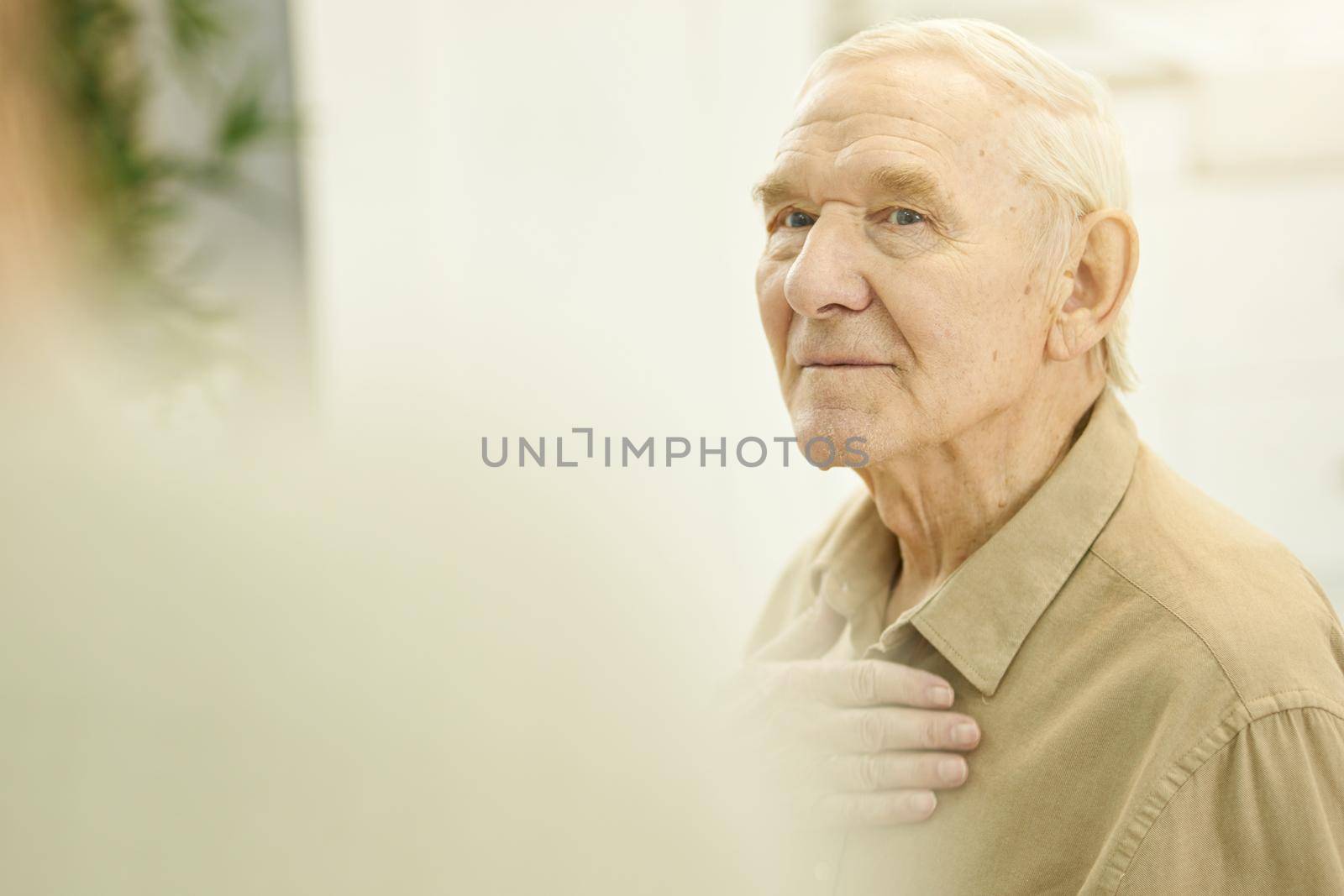 Reserved elderly man touching his chest and looking concerned by friendsstock