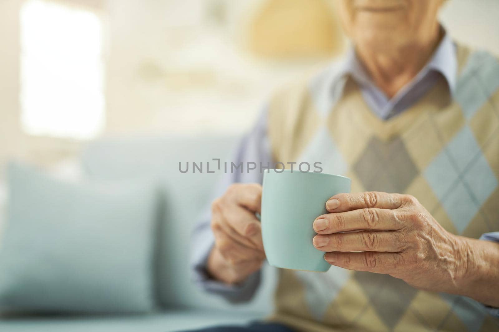 Cropped photo of old-aged man enjoying of hot drink while sitting in living room at home. Copy space