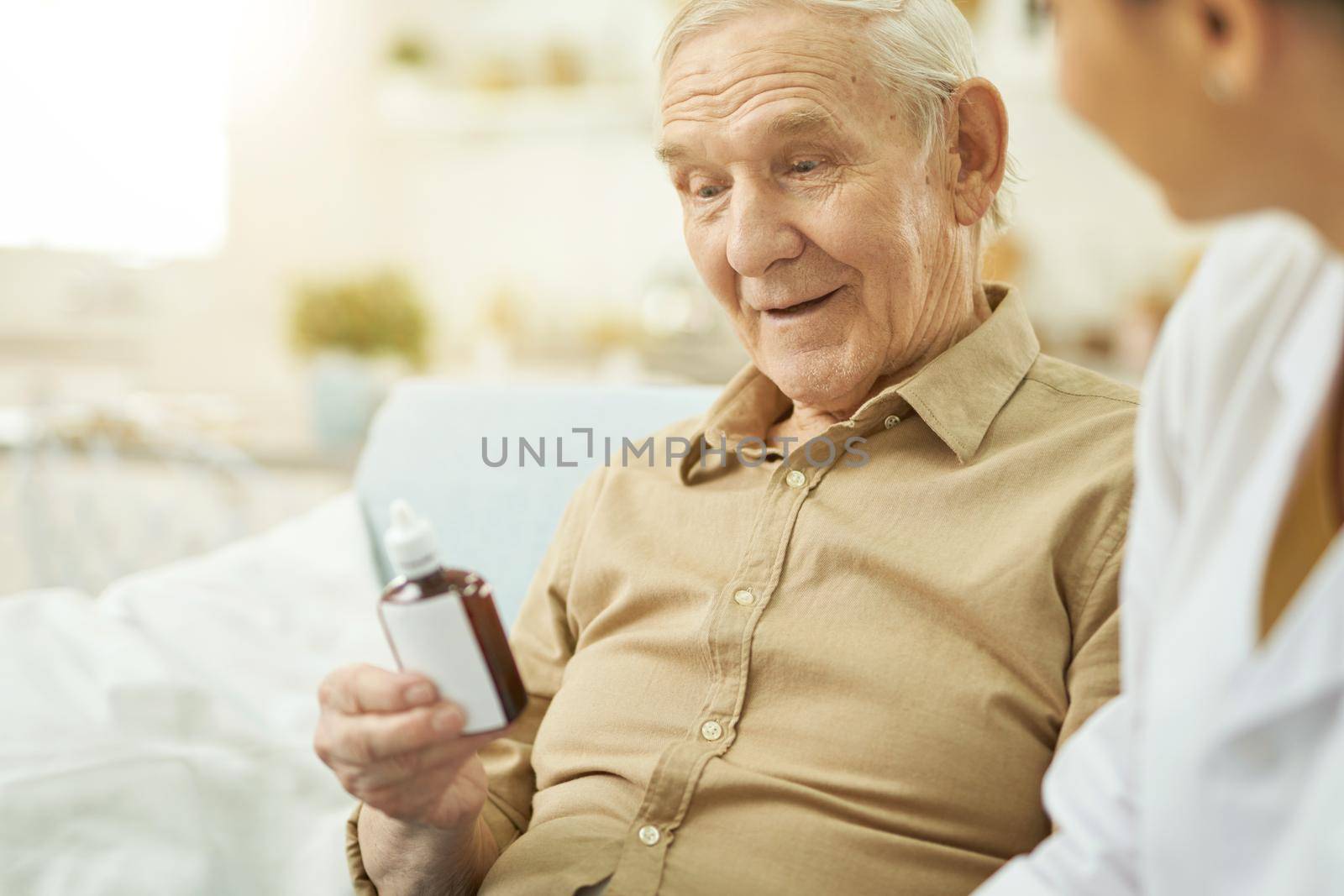 Senior citizen holding medicine and sitting near nurse in room. Copy space