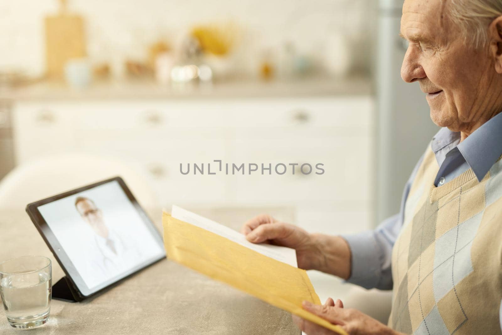 Copy-space photo of an eldelry man holding a yellow parcel while contacting his doctor online