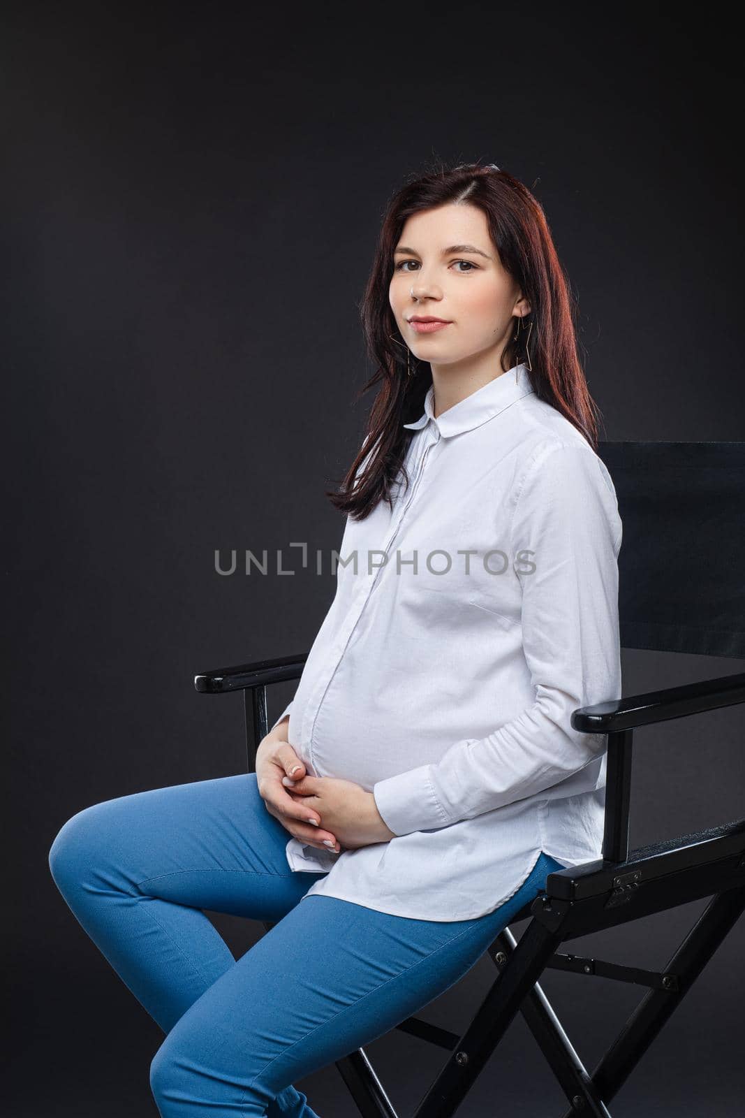 beautiful pregnant mum posing for the camera on a chair in the dark studio