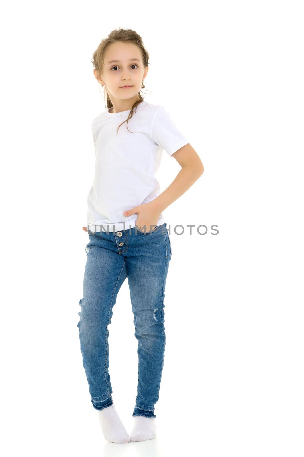 Beautiful Girl Standing with Hands on Her Waist, Cute Child in Blank White Shirt and Blue Jeans Standing Half Turn and Smiling at the Camera, Pretty Girl Posing Against White Studio Background