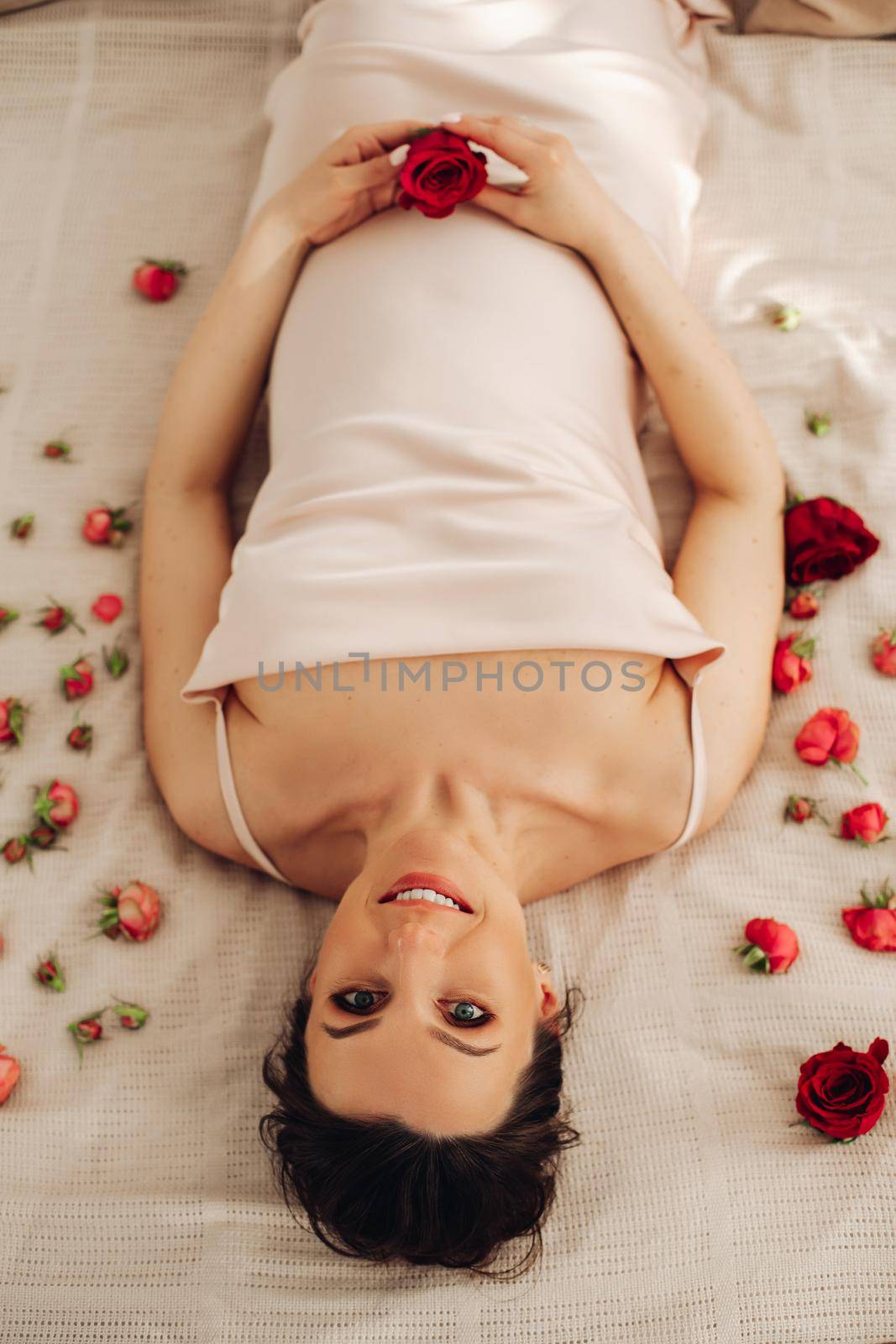 Pregnant woman holds red rose near belly as symbol of new life, wellbeing, fertility. Pregnancy, maternity, gynecology by StudioLucky