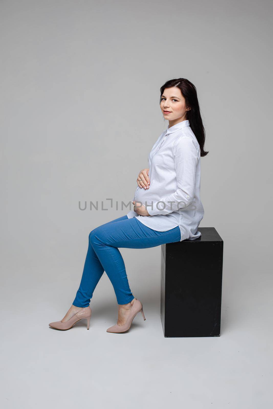 Beautiful pregnant office worker in heels embracing belly. by StudioLucky