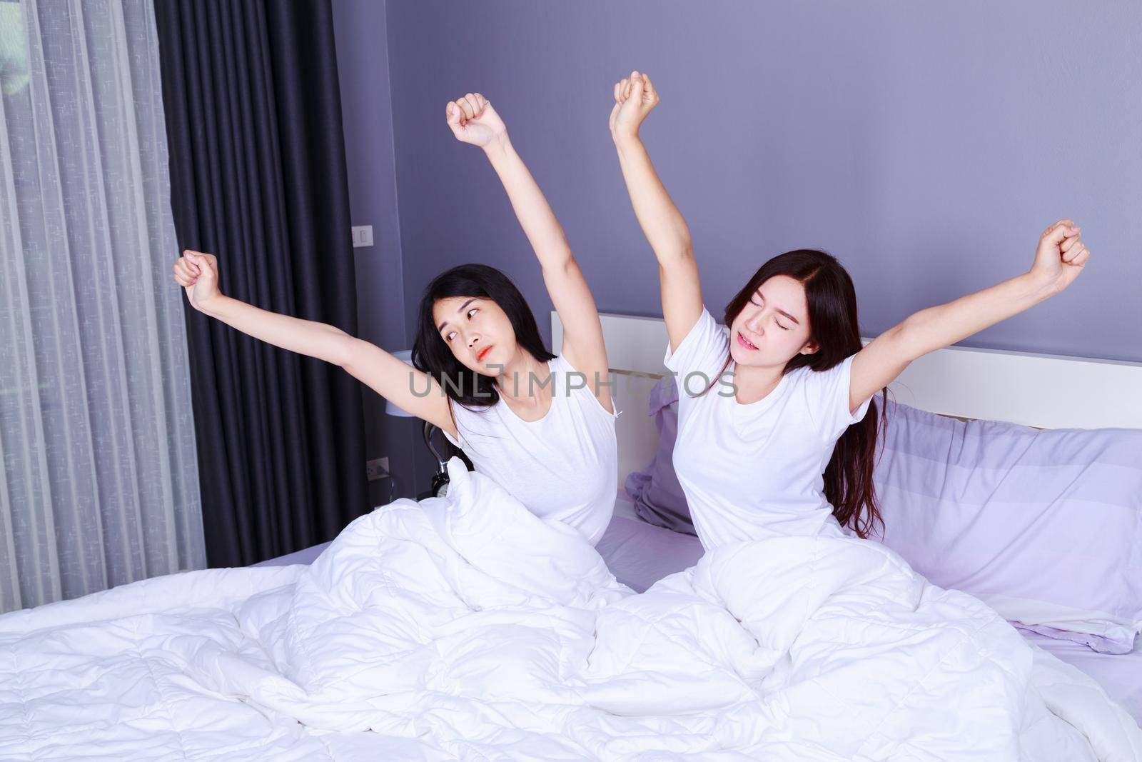 two woman waking up and hand raised on bed in the bedroom