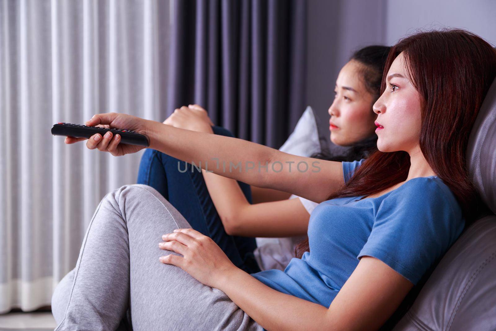 two best friends watching tv with remote on sofa in living room at home