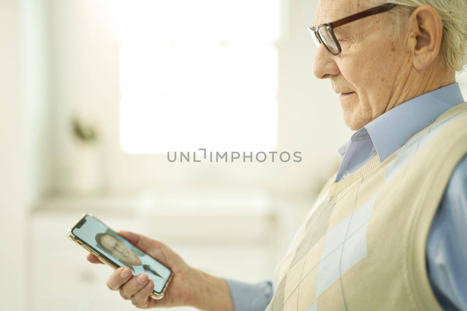 Cropped photo of an aged man in glasses holding a smartphone while consulting his physician via video call