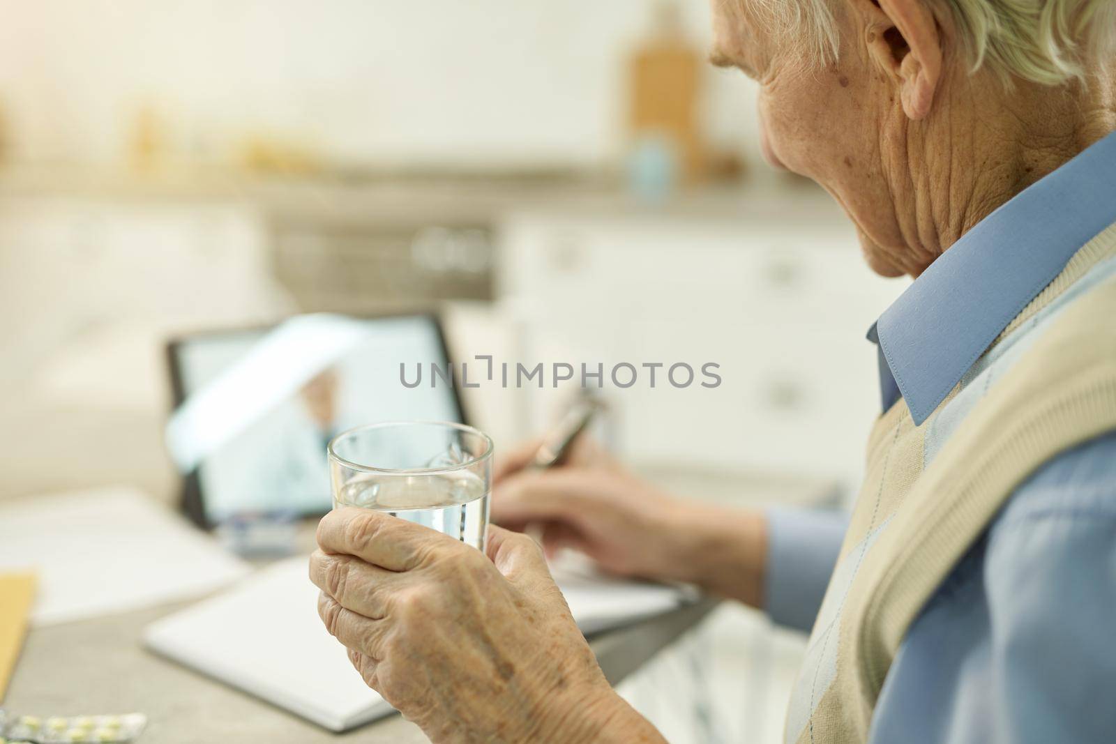 Cropped photo of senior gentleman with glass of water listening to medical advice on an online consultation