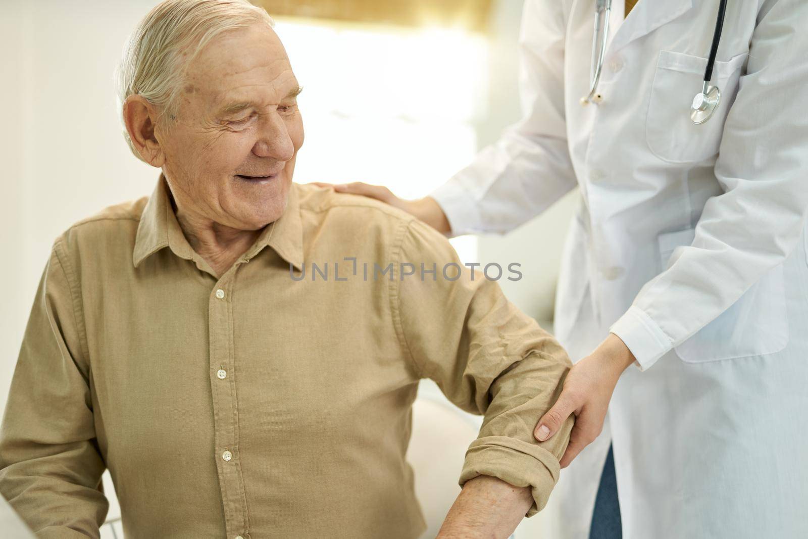 Mirthful elderly man being helped up by medical staff by friendsstock