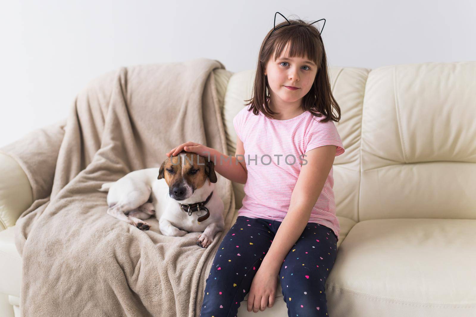 Child girl with cute dog jack russell terrier on the couch. Pets and home.