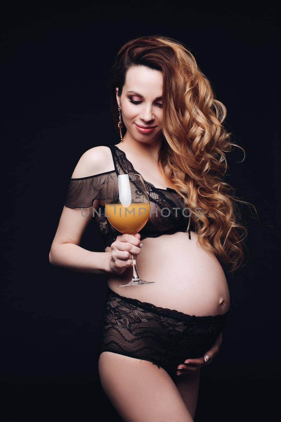 Waist up of happy pretty pregnant lady in black lingerie while posing in studio isolated on black background