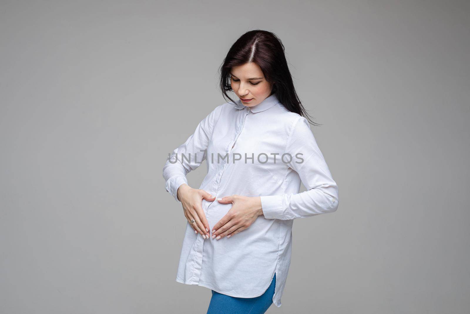 Pregnant girl show heart shape gesture on belly waiting for baby. Maternity concept. Expectant mother during pregnancy. High quality photo