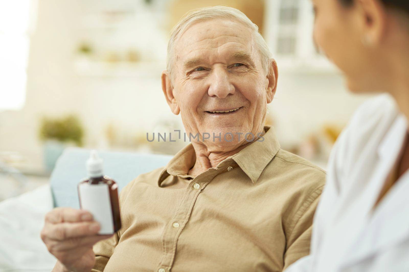 Smiling senior citizen looking at nurse and holding medicine while sitting at home