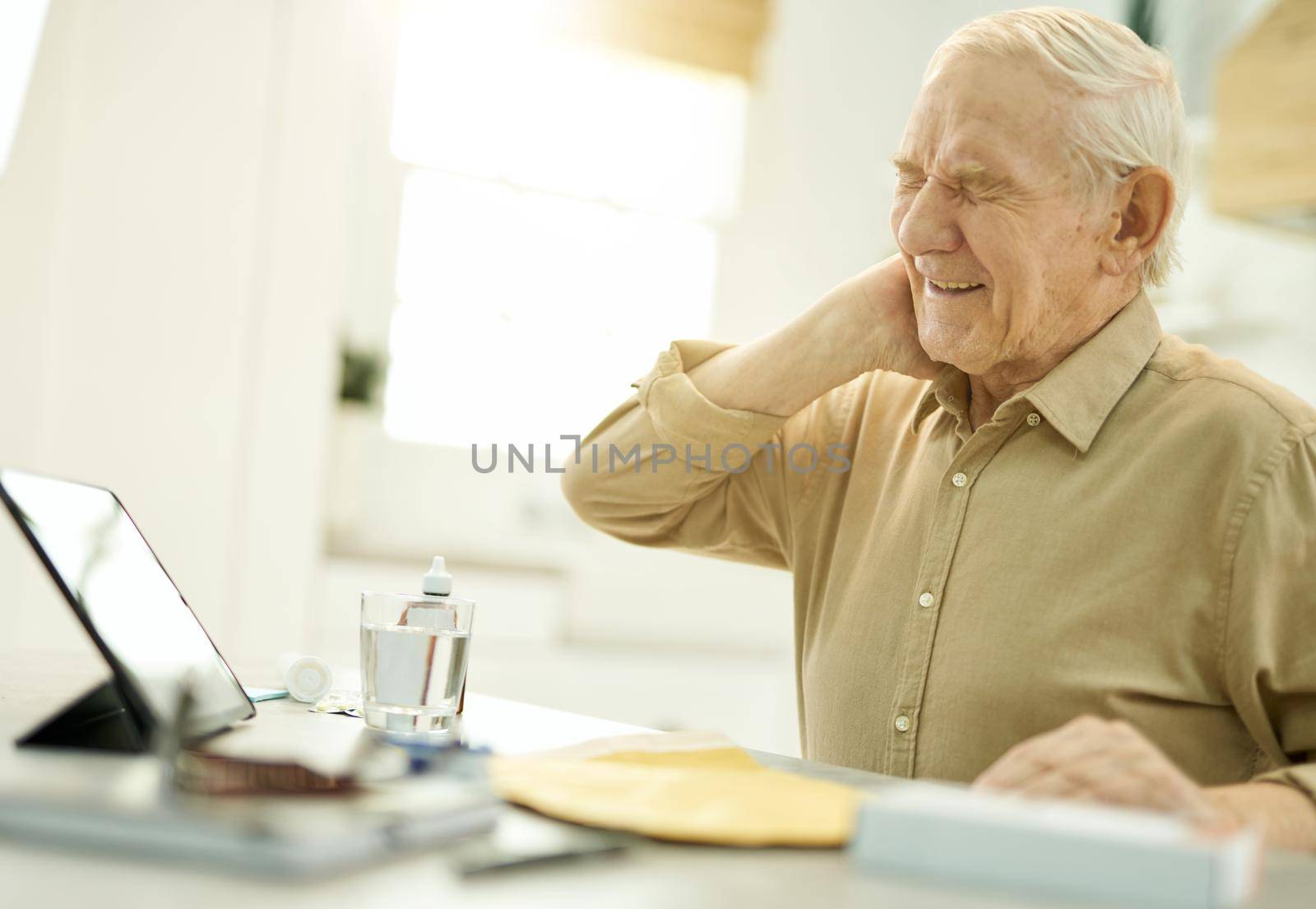 Distressed elderly man cringing in pain while touching his neck while getting medical consultation online