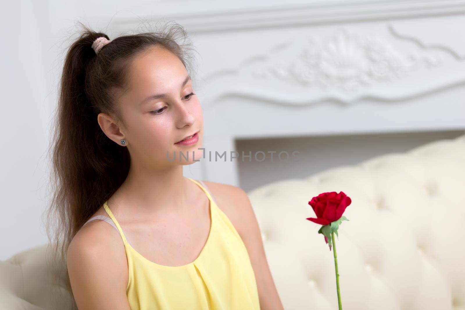 Very beautiful teen girl sitting on a couch holding a flower in her hand. The concept of style and fashion.