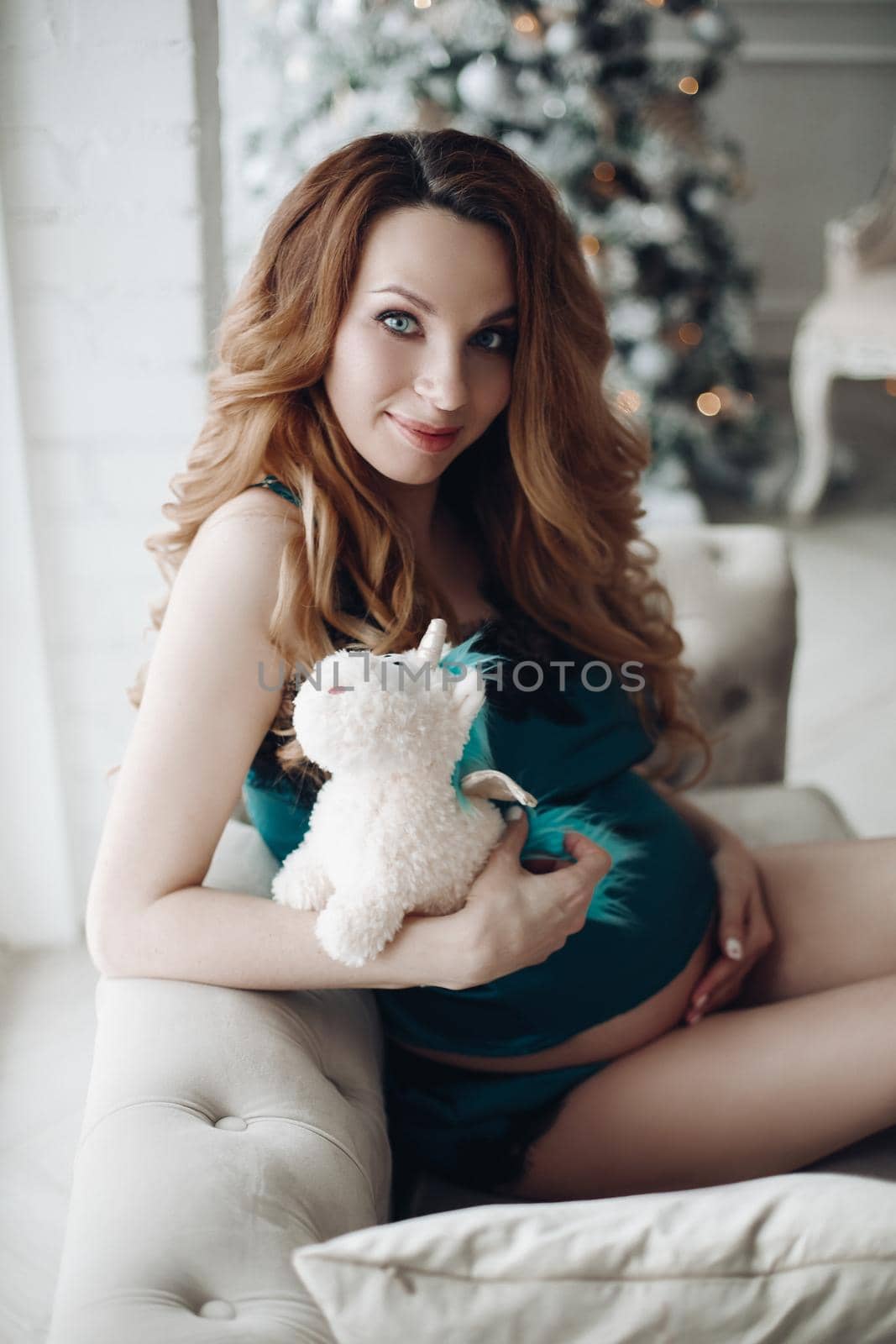 Beautiful fashion pregnancy young girl in pajamas posing at Christmas tree background by StudioLucky