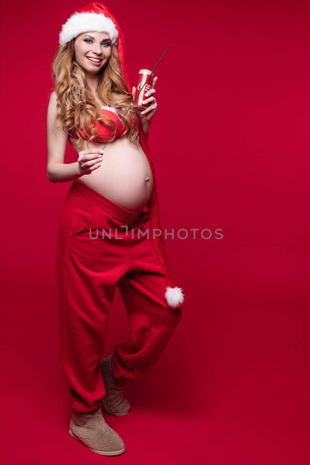 11 27 2019 Belarus Minsk: Smiling pretty pregnant lady touching the abdomen in studio by StudioLucky