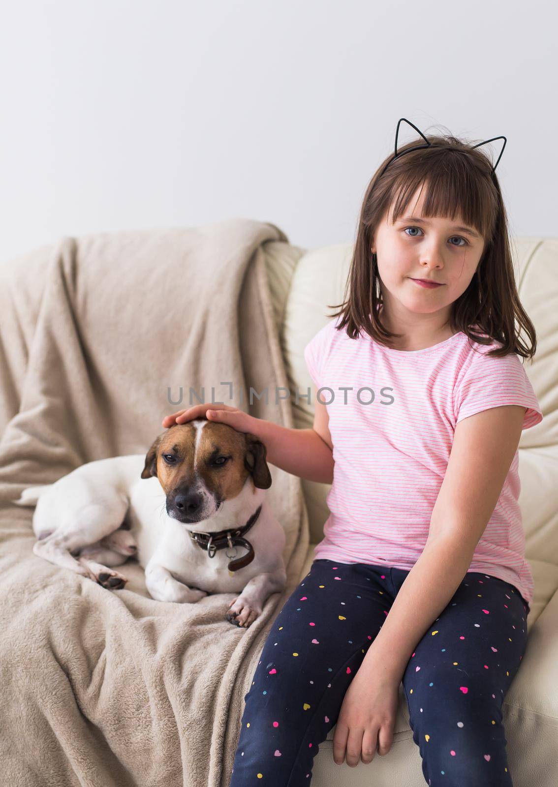 Child girl with cute dog jack russell terrier on the couch. Pets , children and home concept. by Satura86