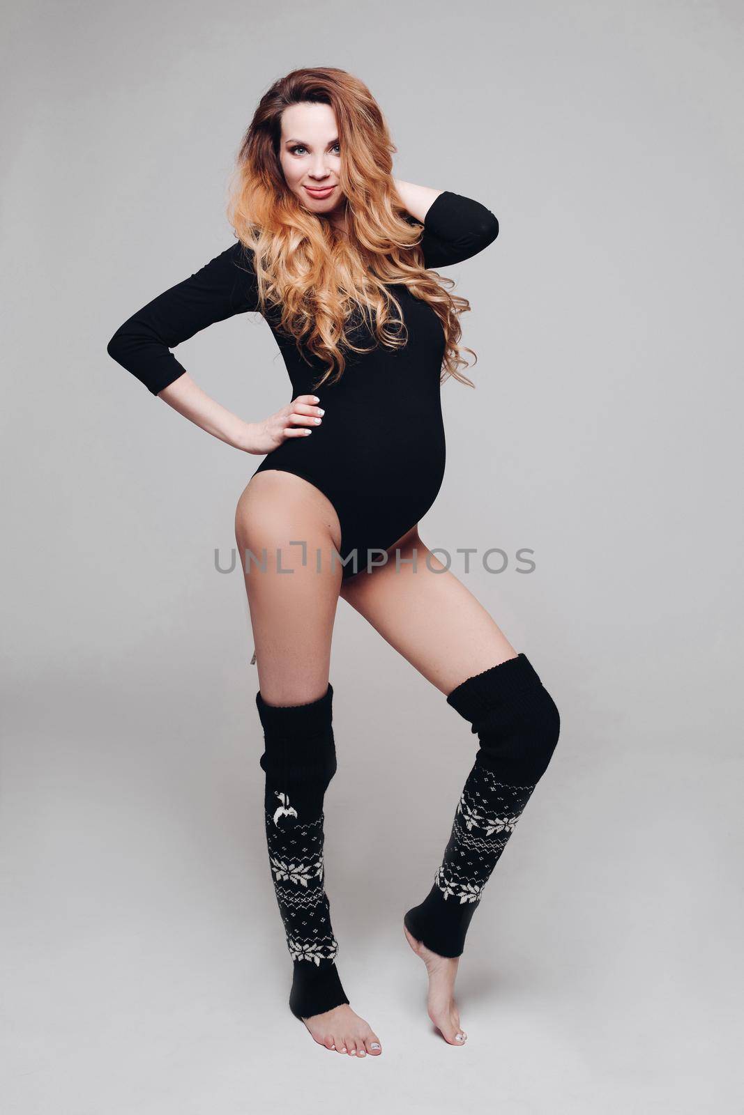 Charming fitness smiling pregnancy woman in black body and gaiters posing having positive emotion. Beautiful active pregnant female enjoying motherhood isolated at white studio background full shot