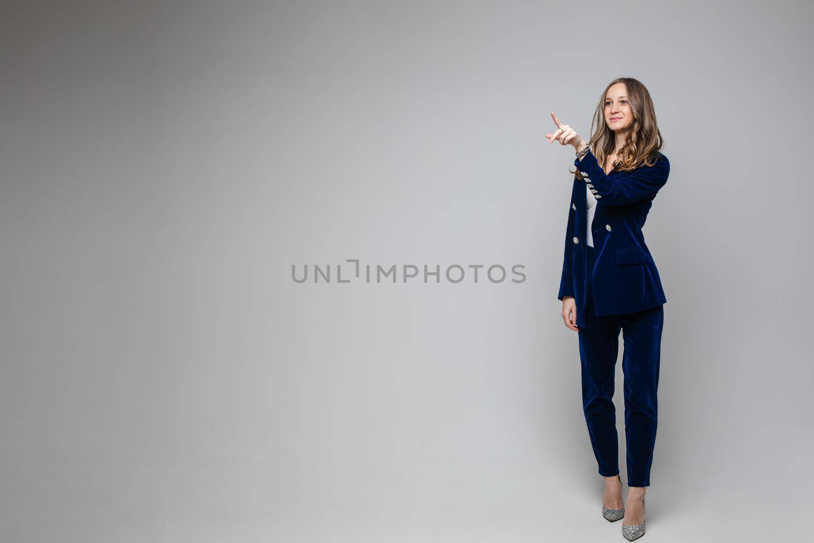 Friendly positive young girl in blue suit uniform pointing on blank space on gray background for advertising content by StudioLucky