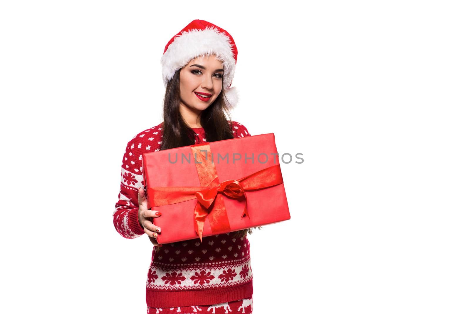 Young woman with long beautiful hair in Santa hat and New Year's dress holding Christmas present in her hands isolated on white background. Christmas sale. Emotional brunette. Copy space
