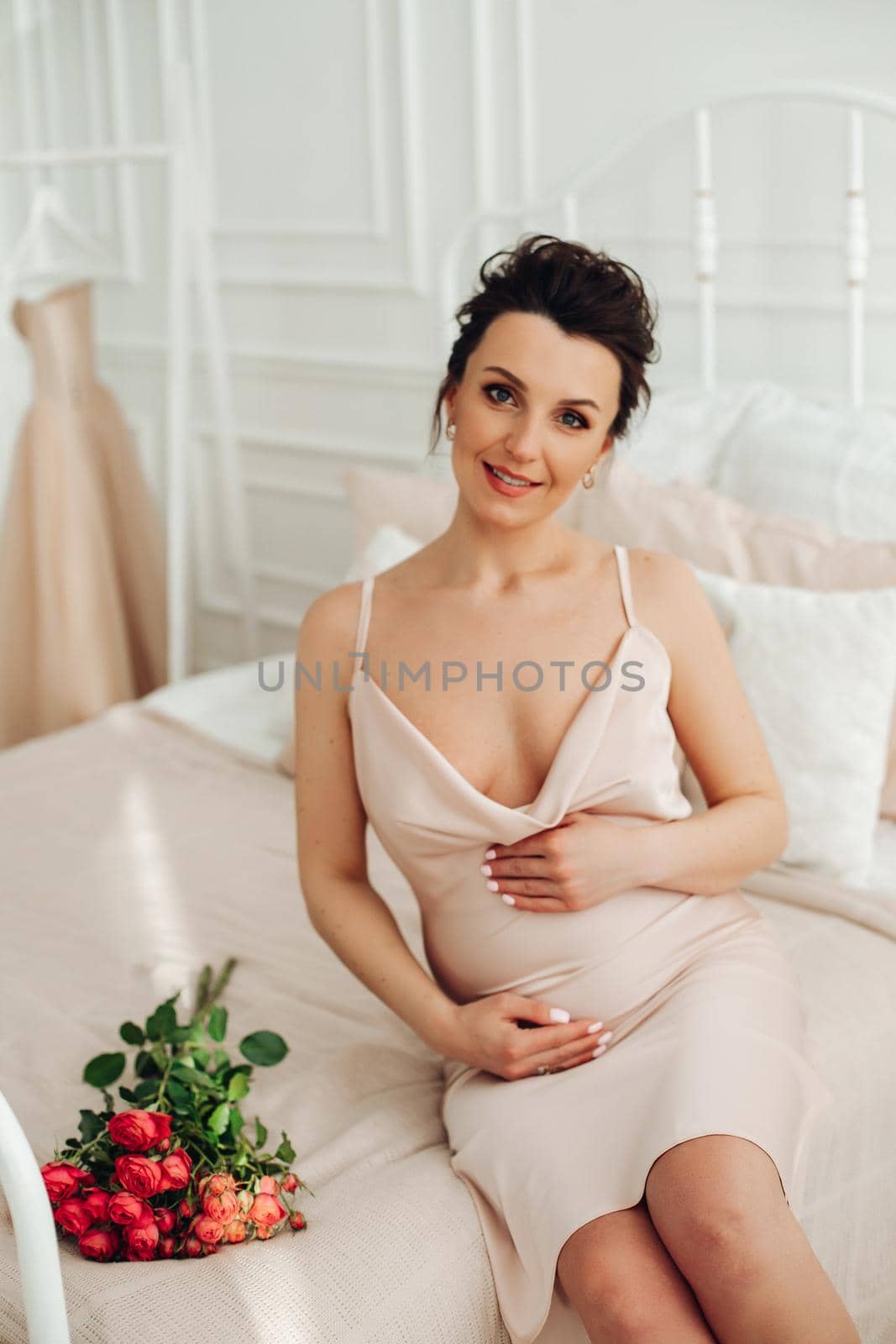 attractive pregnant woman in silk dress touches her belly with happy smile by StudioLucky