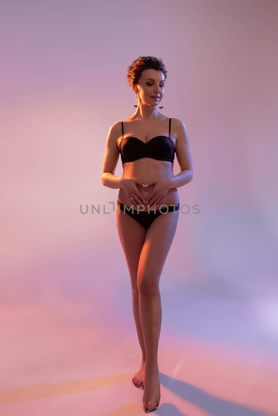 attractive pregnant woman in underwear touches her belly and looking aside by StudioLucky