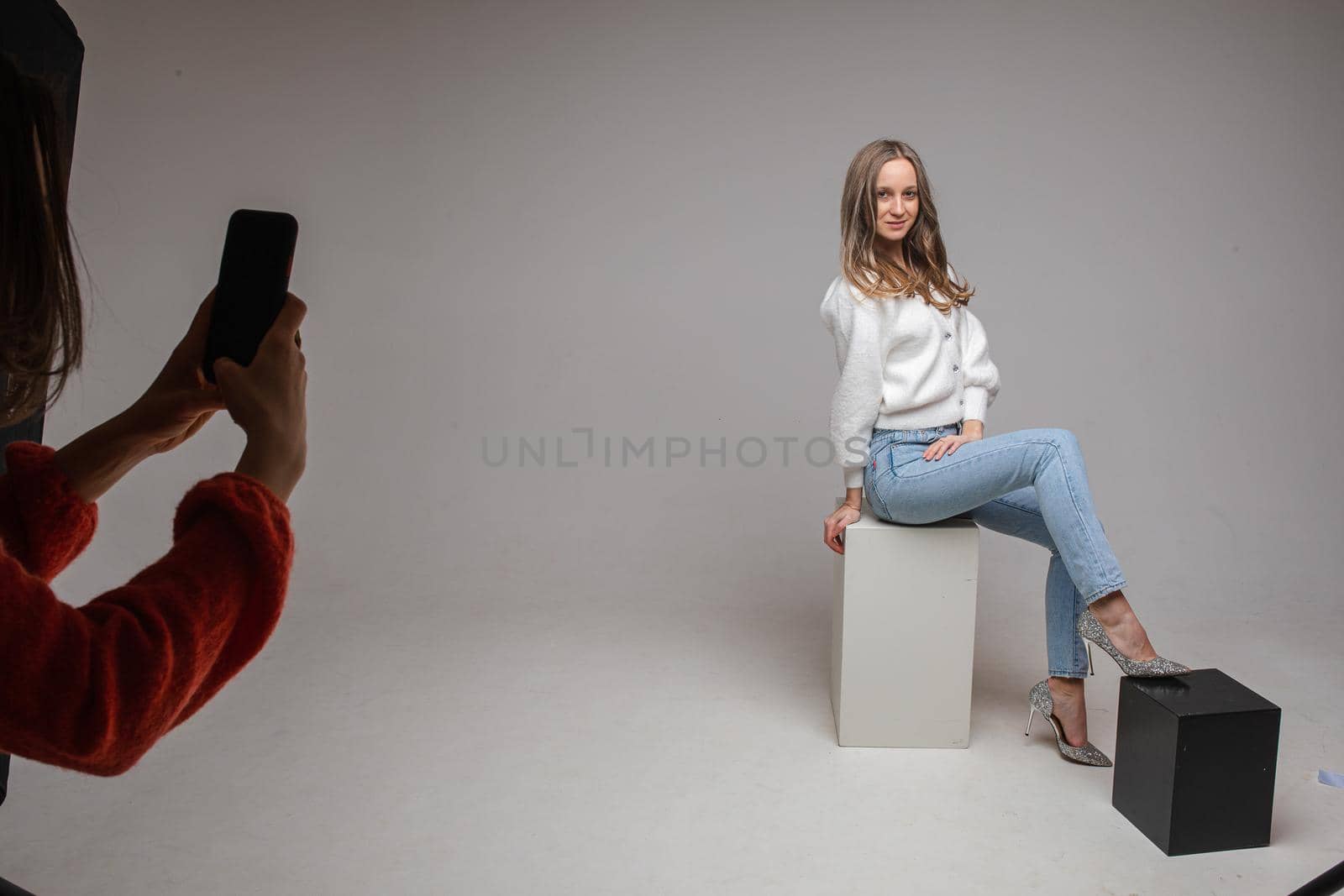 caucasian woman with attractive appearance sits on a white cube, picture isolated on white background