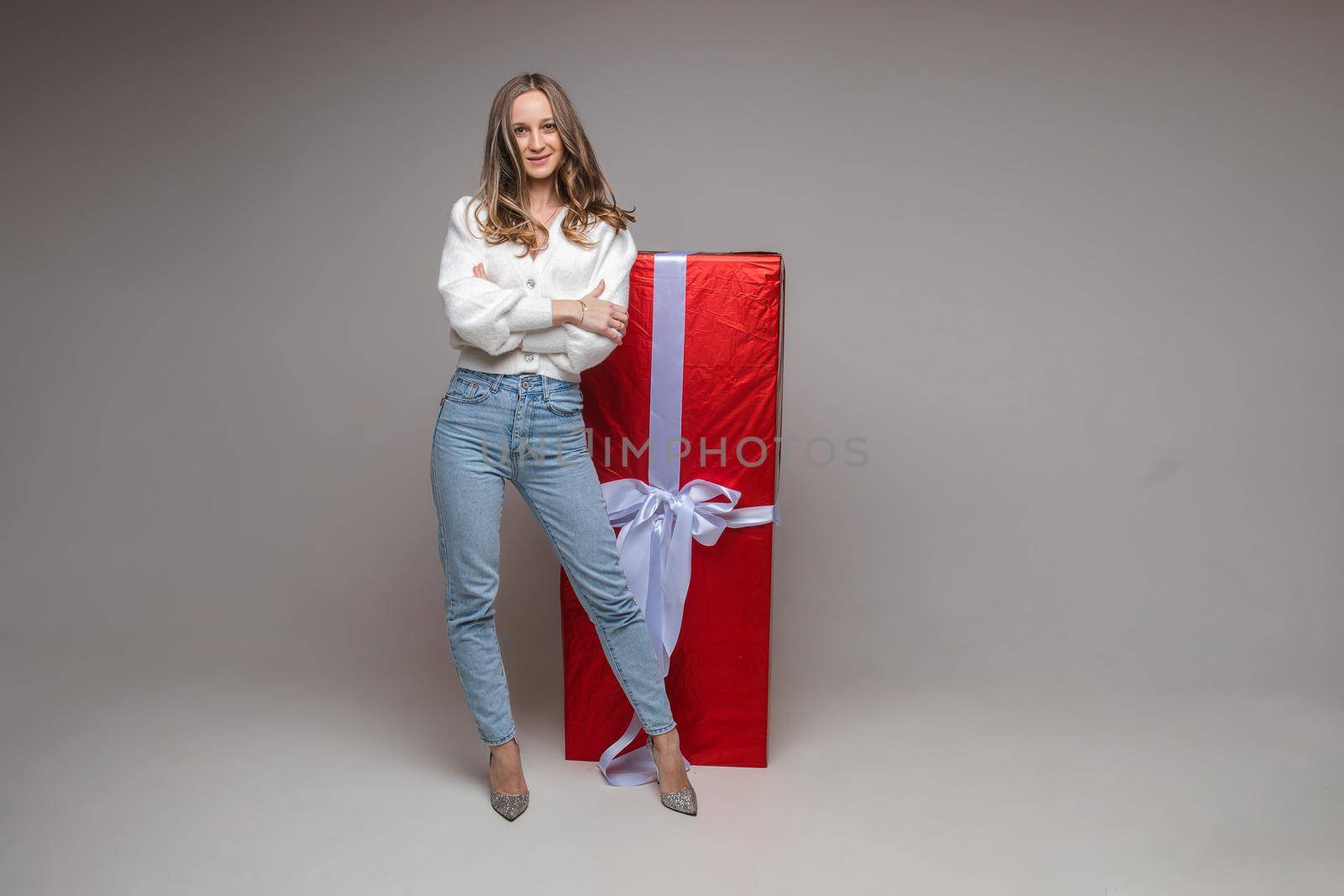 Pretty fit young girl with big red gift on gray studio background with copy space for holiday advertising by StudioLucky