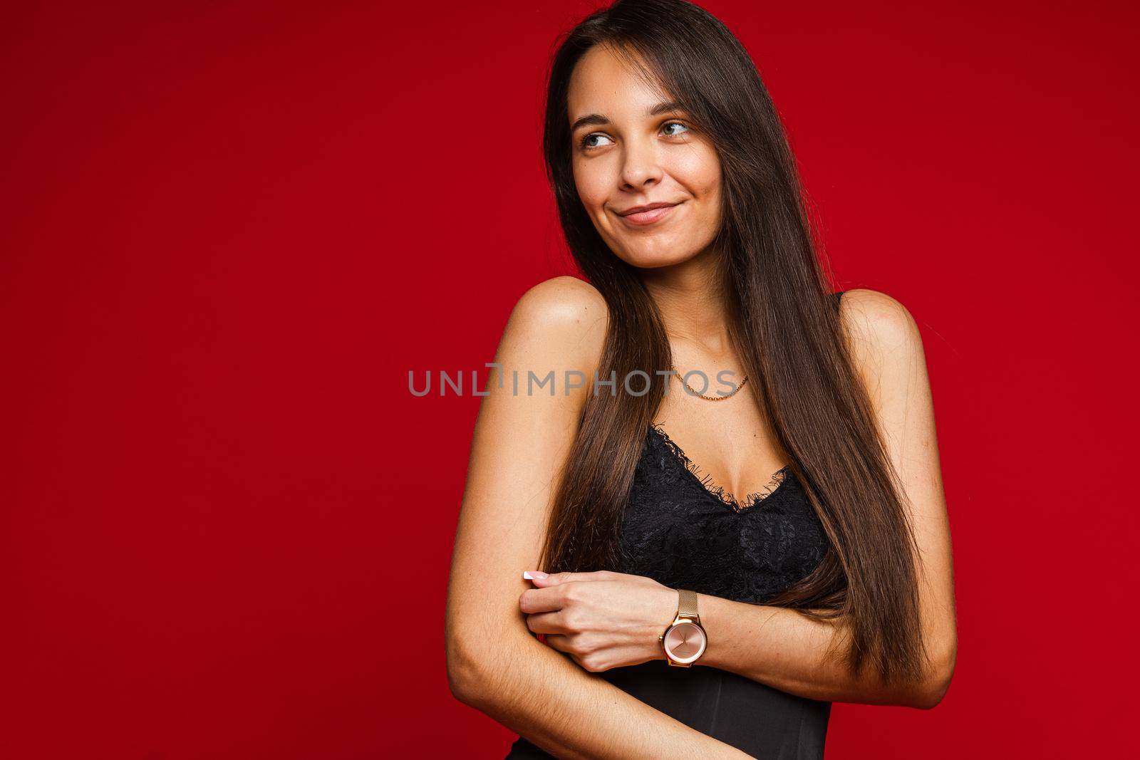 Studio portrait of attractive smiling woman with long straight brown hair in black top with lace design posing on red background. Copy space.