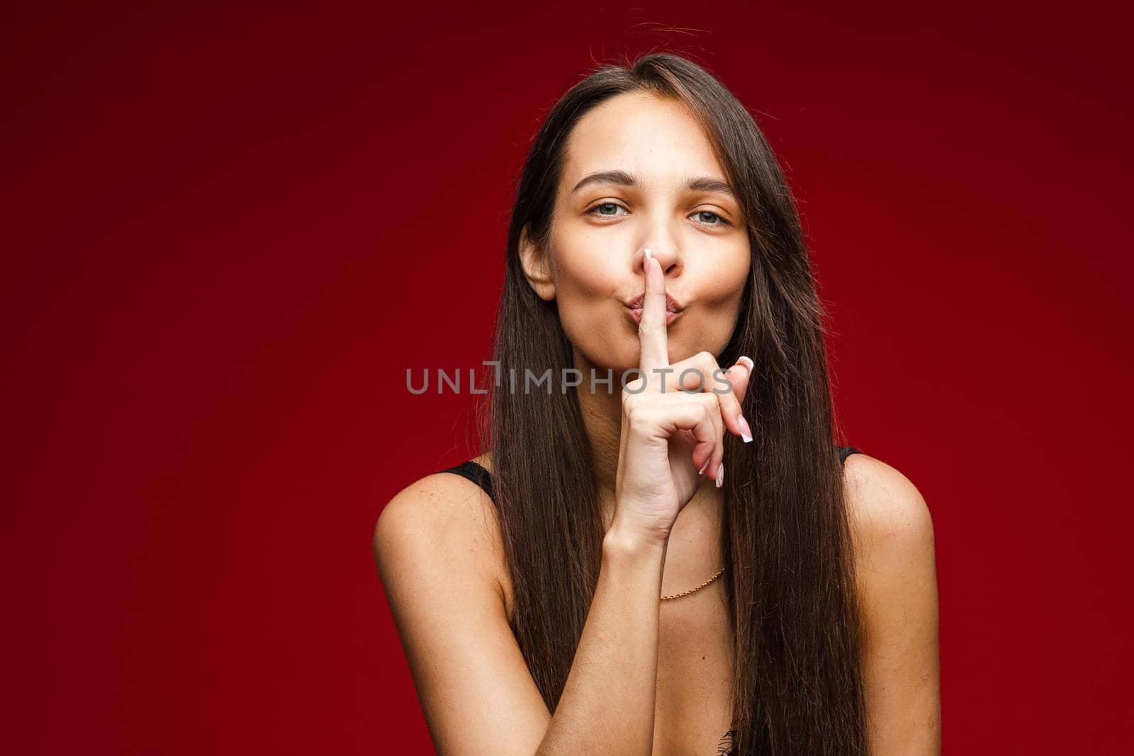 ccaucasian woman with attractive appearance shows that youn should be quiet, picture isolated on red background