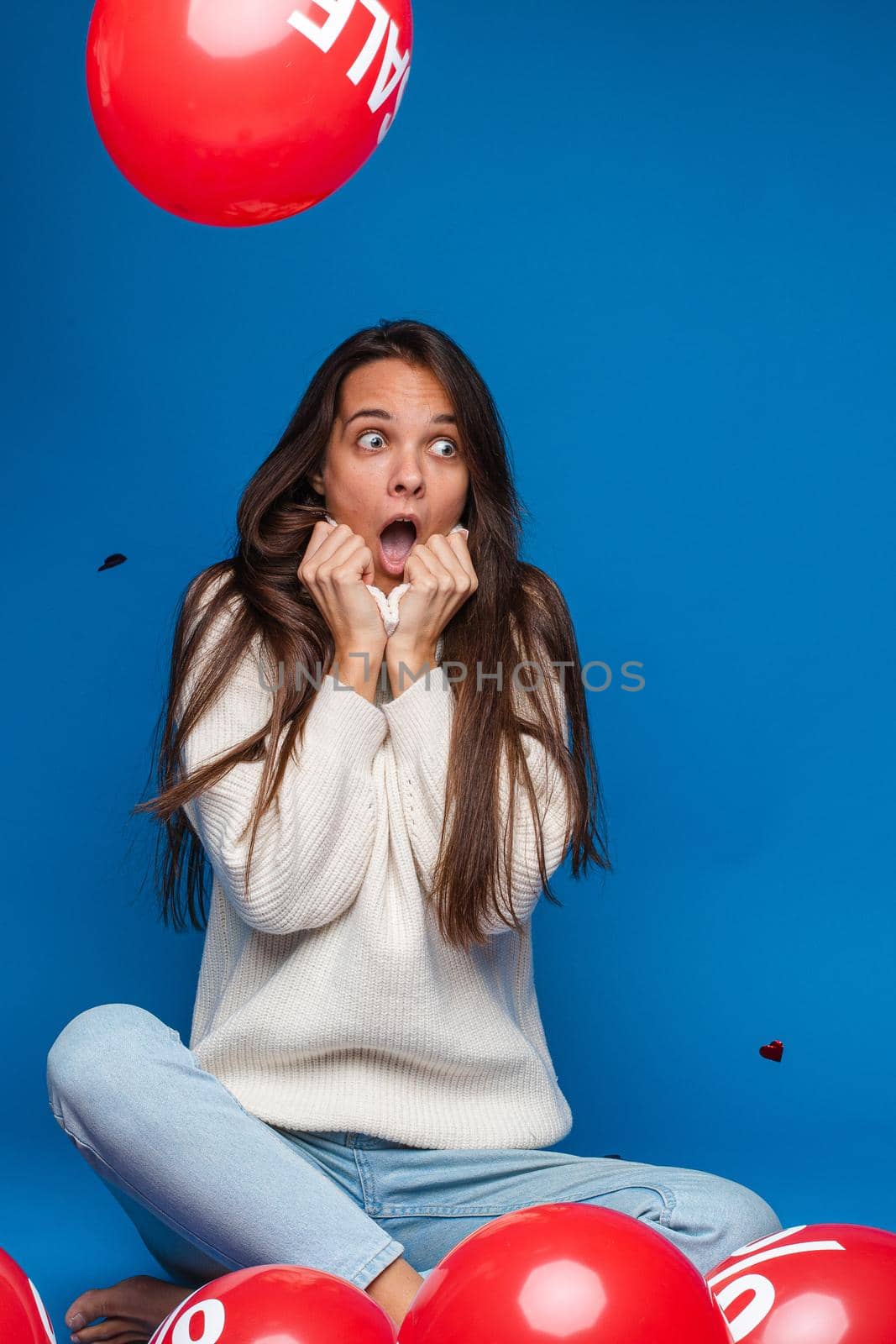 caucasian woman with attractive appearance sits with baloons with percent print is in shock, picture isolated on blue background