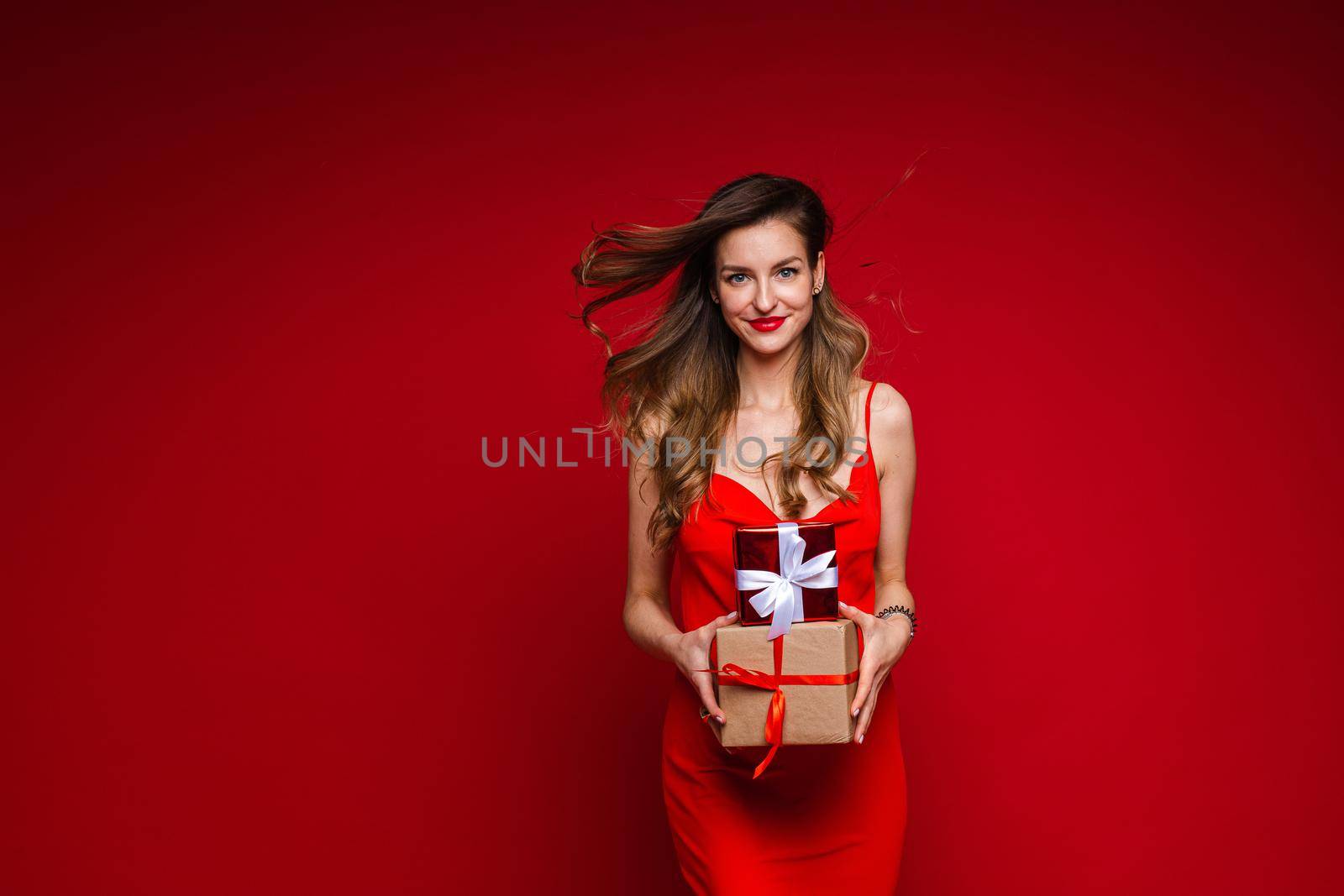 beautiful female fashion model in red dress holds a lot of small boxes with presents and rejoices by StudioLucky