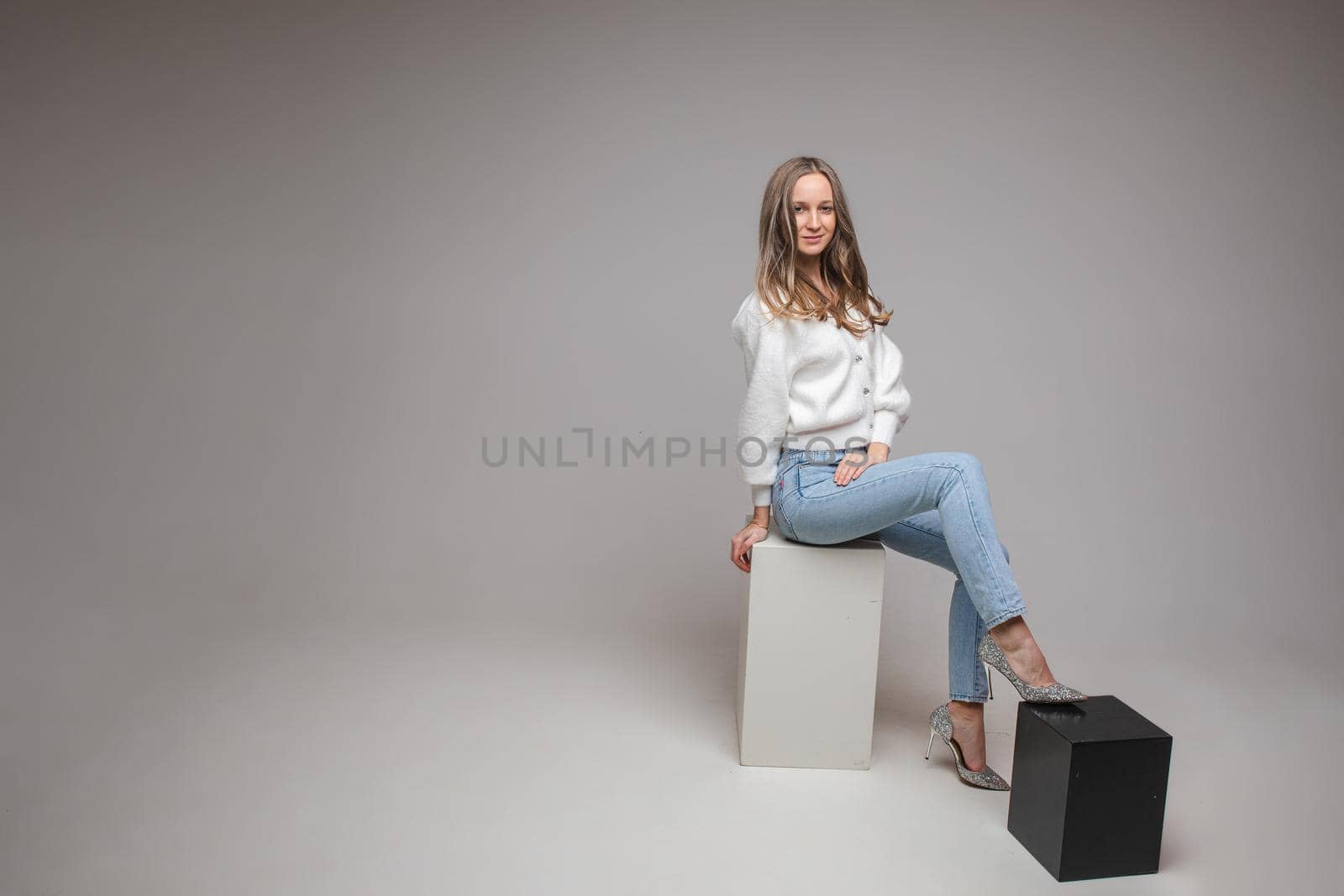 caucasian woman with attractive appearance sits on a white cube, picture isolated on white background