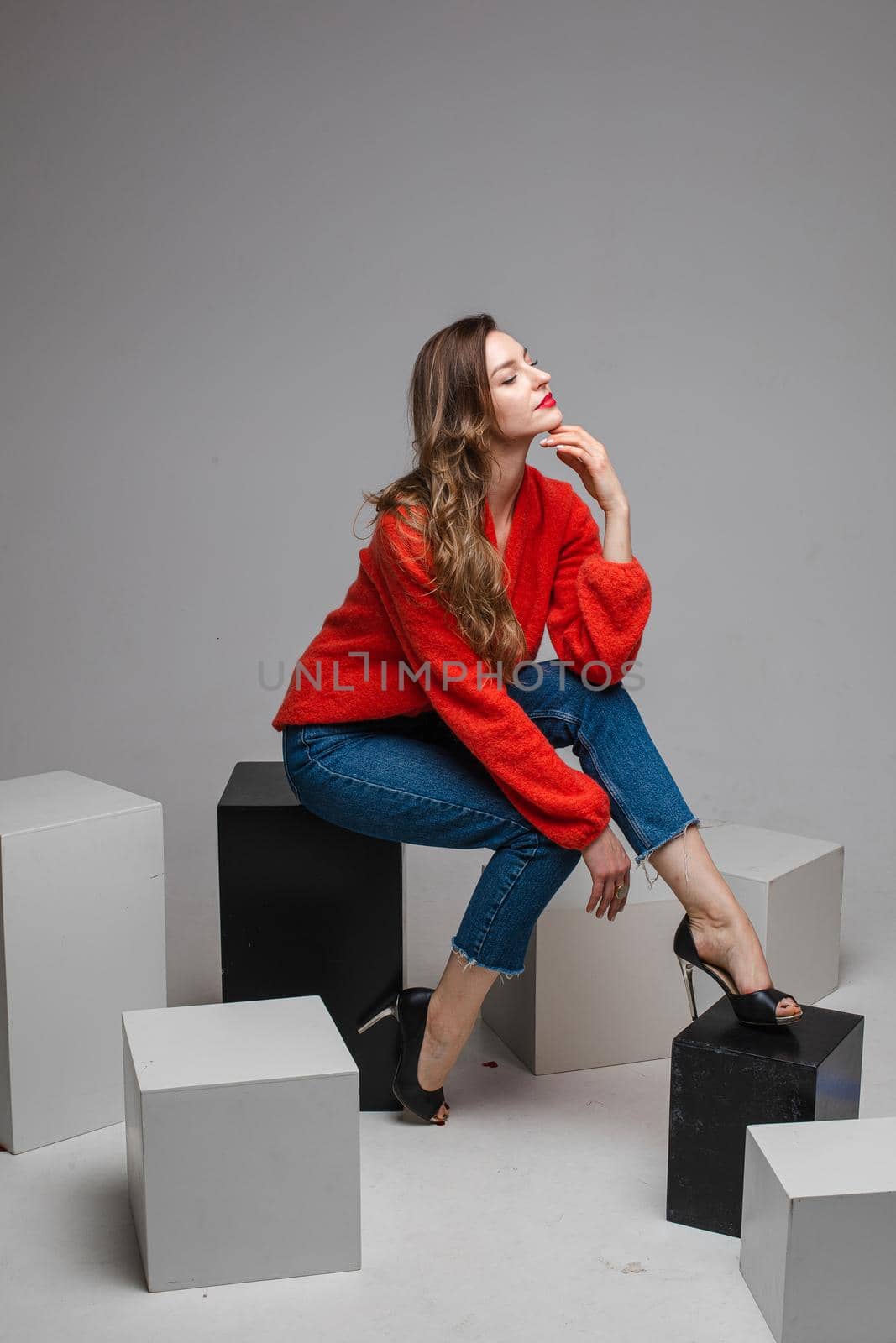 beautiufl caucasian woman with charming appearance sits on a white cube and looks to te camera, picture isolated on white background