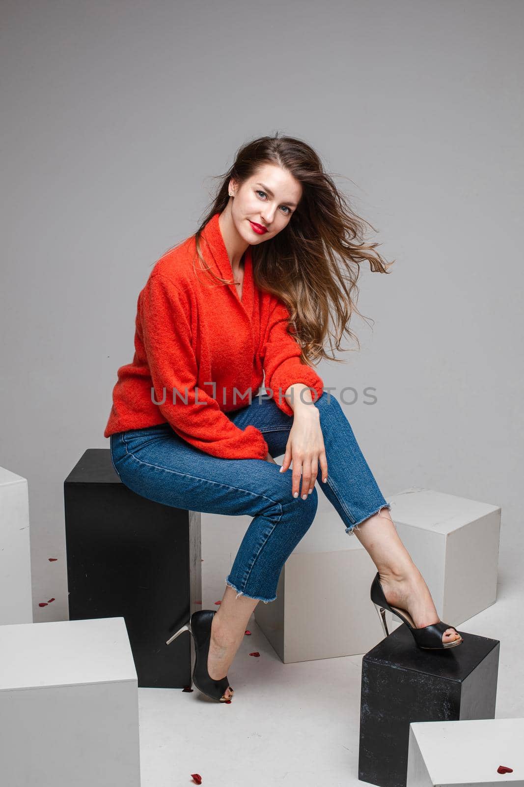 Happy pretty brunette lady sitting on the black rectangle chair, isolated on grey background. Copy space