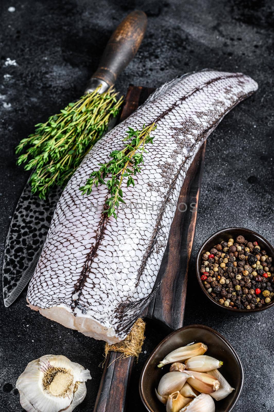 Raw grenadier macrurus white fish on a wooden cutting board. Black background. Top view.