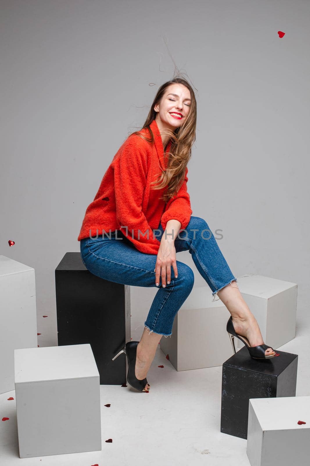 beautiuful caucasian woman sits on a white cubes and looks to the camera, picture isolated on white background