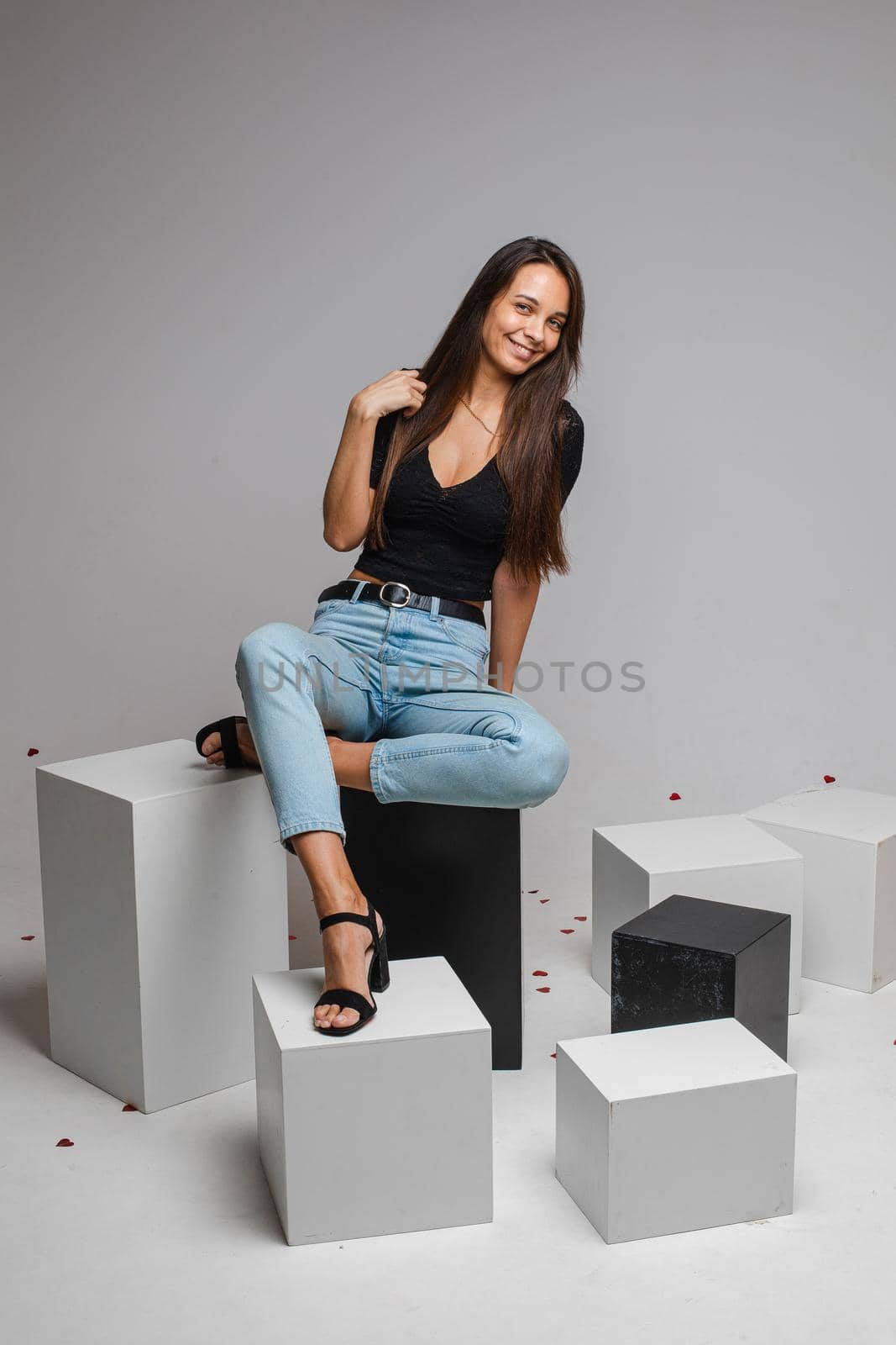 beautiufl caucasian woman with charming appearance sits on a white cube and looks to te camera, picture isolated on white background